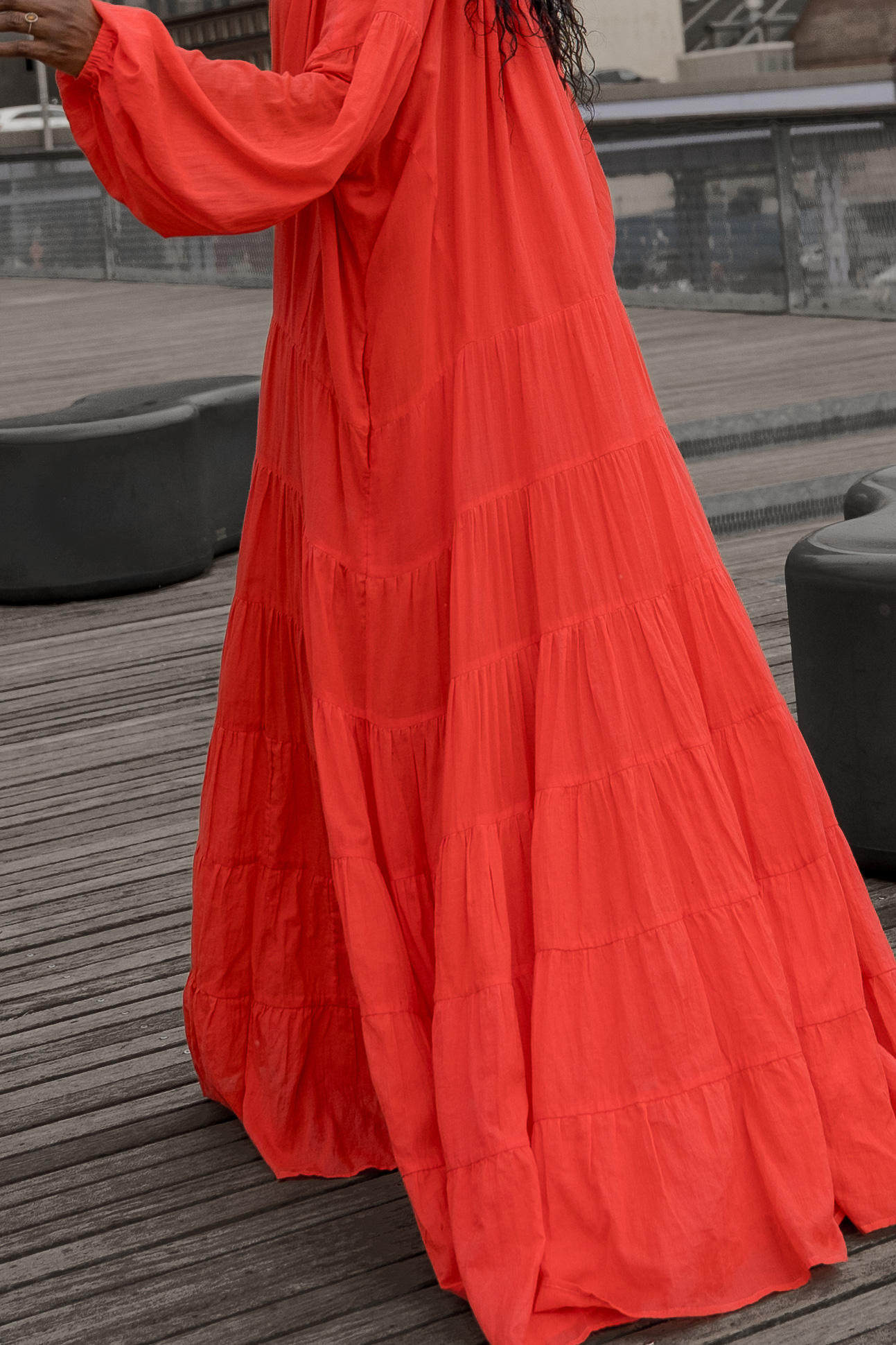 Woman in a red maxi dress poses on a pier at the South Street Seaport in New York City with a view of the skyline and water.