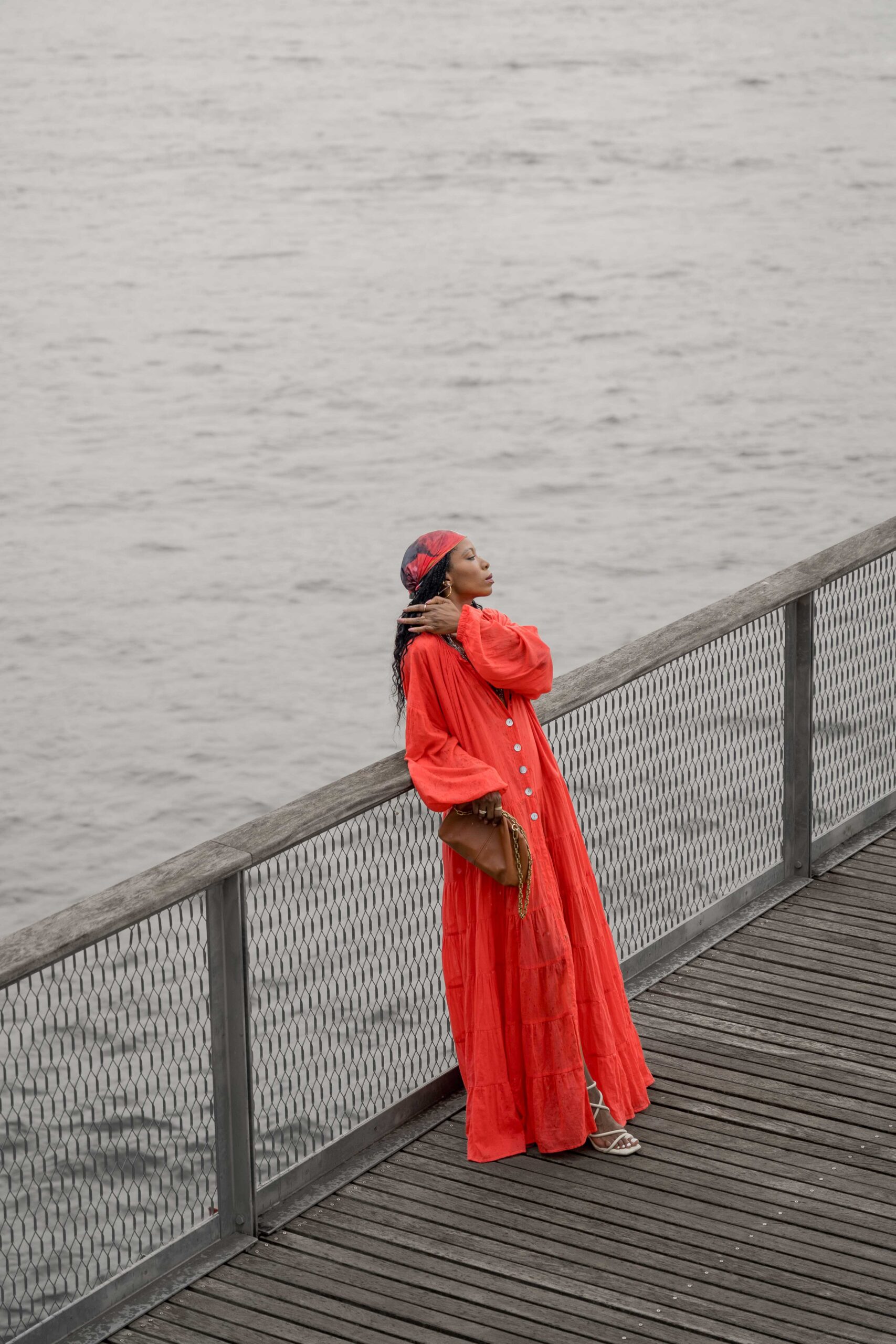 Woman in a red maxi dress poses on a pier at the South Street Seaport in New York City with a view of the skyline and water.