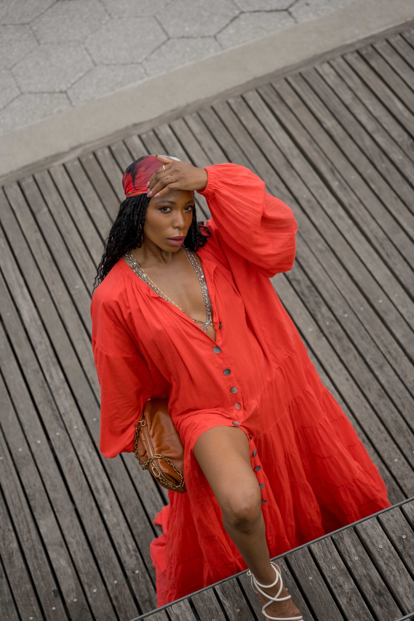 Woman in a red maxi dress poses on a pier at the South Street Seaport in New York City with a view of the skyline and water.