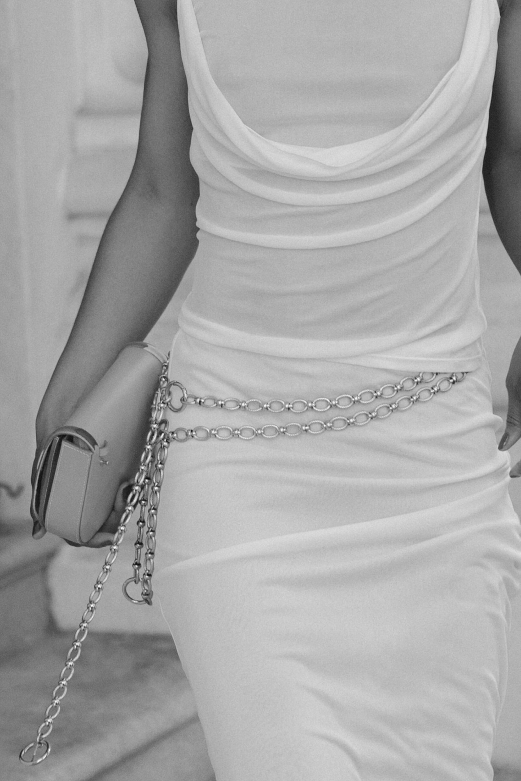 A stylish outfit: a white maxi skirt set, silver chain belts, and black heels, worn by a woman on a New York City street.