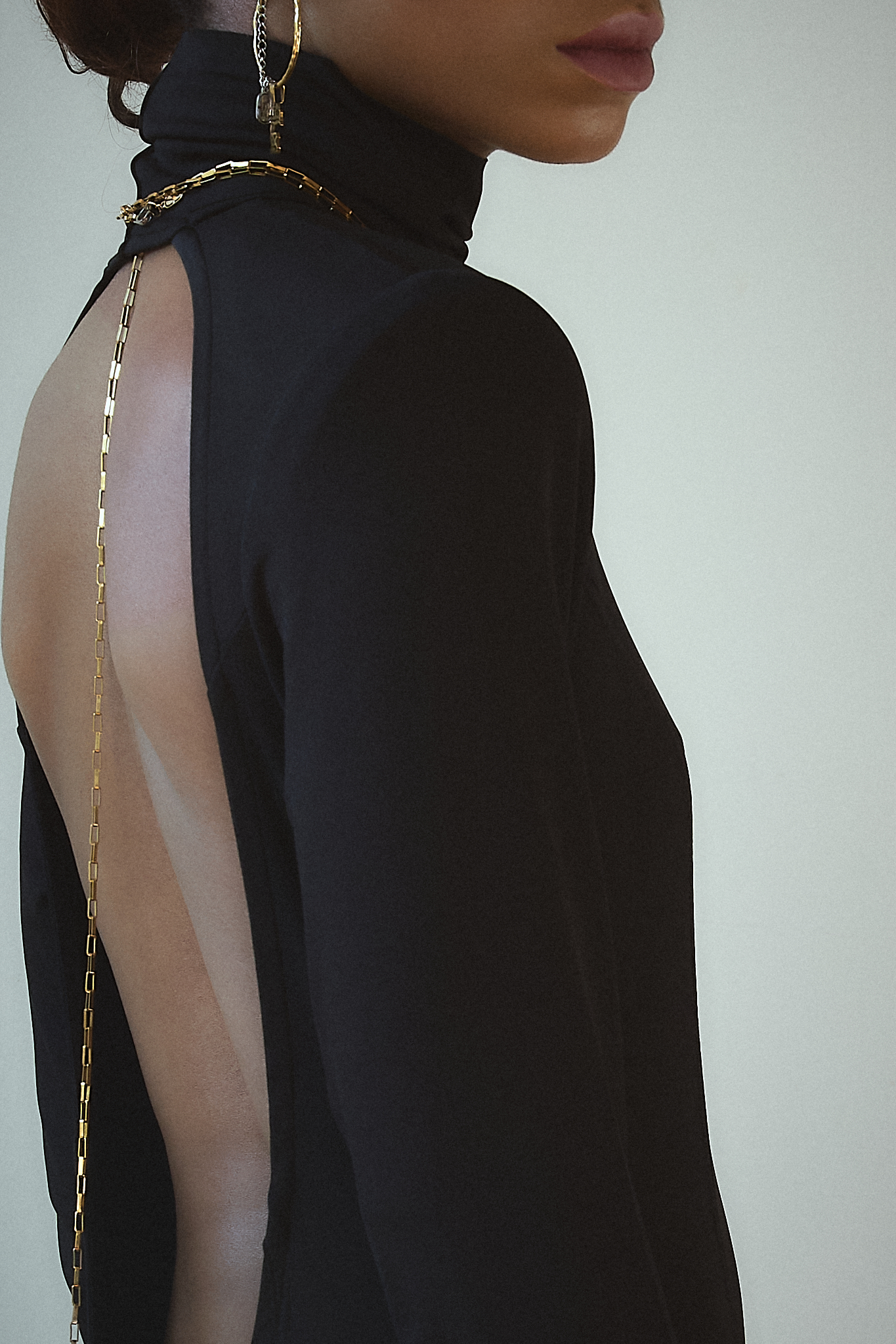 Close-up of the back of a black backless maxi dress, highlighting a delicate gold chain draped along the spine for an elegant touch.