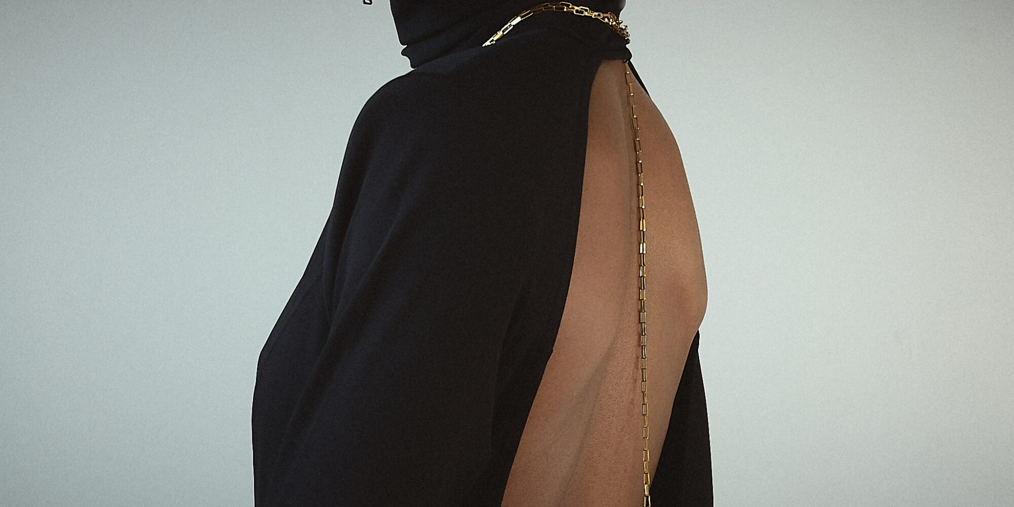 Close-up of the back of a black backless maxi dress, highlighting a delicate gold chain draped along the spine for an elegant touch.