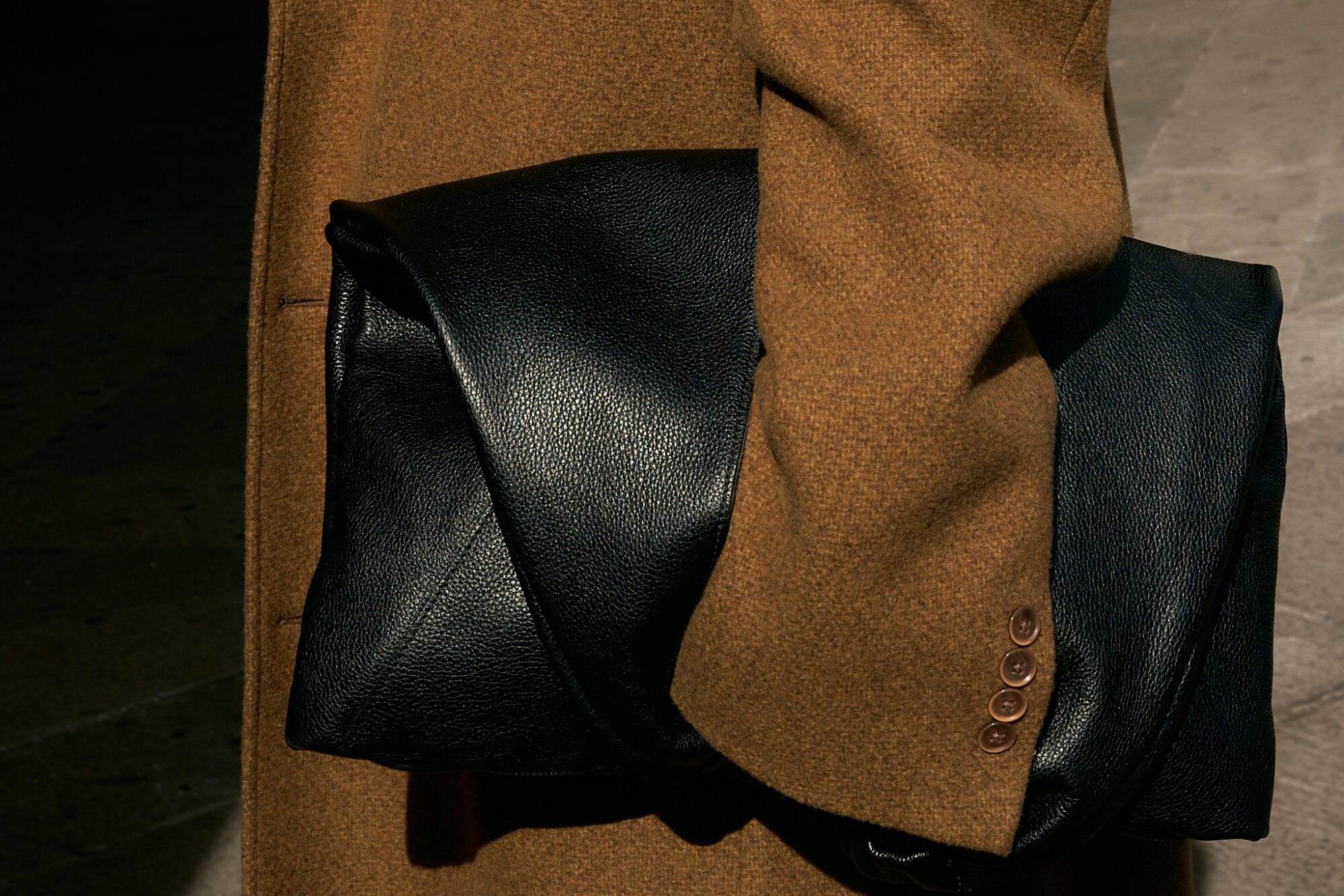 She wears a chic minimalist outfit. A black button-down shirt layered over a crisp white turtleneck, creating a sleek and structured base. A black denim maxi skirt with a front slit adds dimension and movement, while a silver chain belt from Lapo Lounge injects a bold, modern edge. The ensemble is topped with a classic camel coat, adding warmth and sophistication to the monochromatic foundation. Accessories complete the look—oversized black sunglasses for a cool, mysterious vibe, gold hoop earrings for a hint of elegance, and a black leather clutch for a polished finish. She grounds the outfit with black and white sneakers, effortlessly blending high fashion with street-style ease.