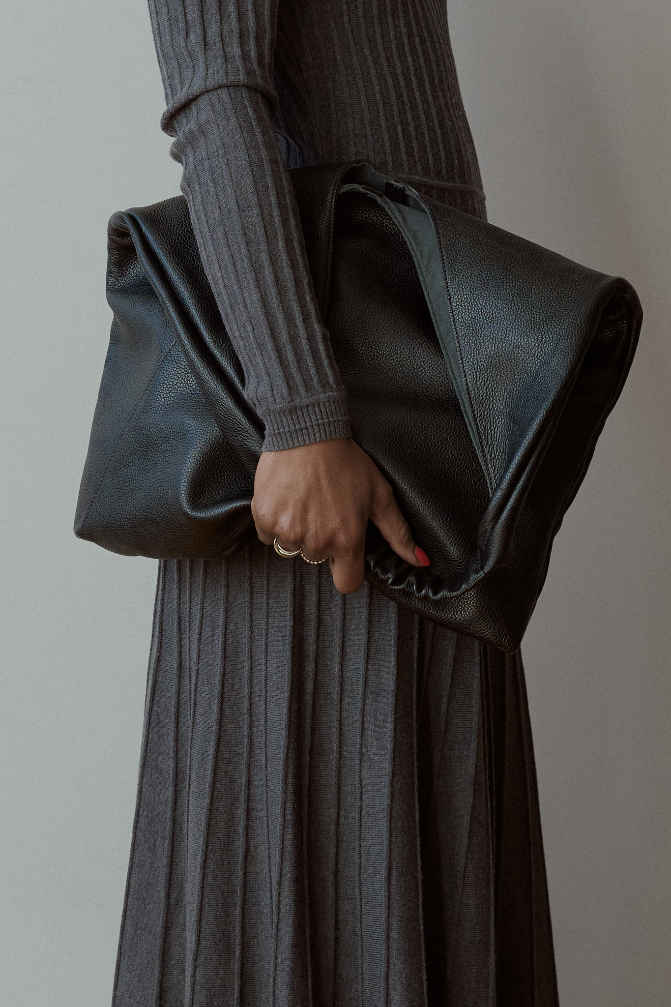 Model wearing a ribbed grey knit maxi dress with an open back and long silver lariat necklace, styled with a black leather clutch — minimalist and elegant winter outfit inspiration.
