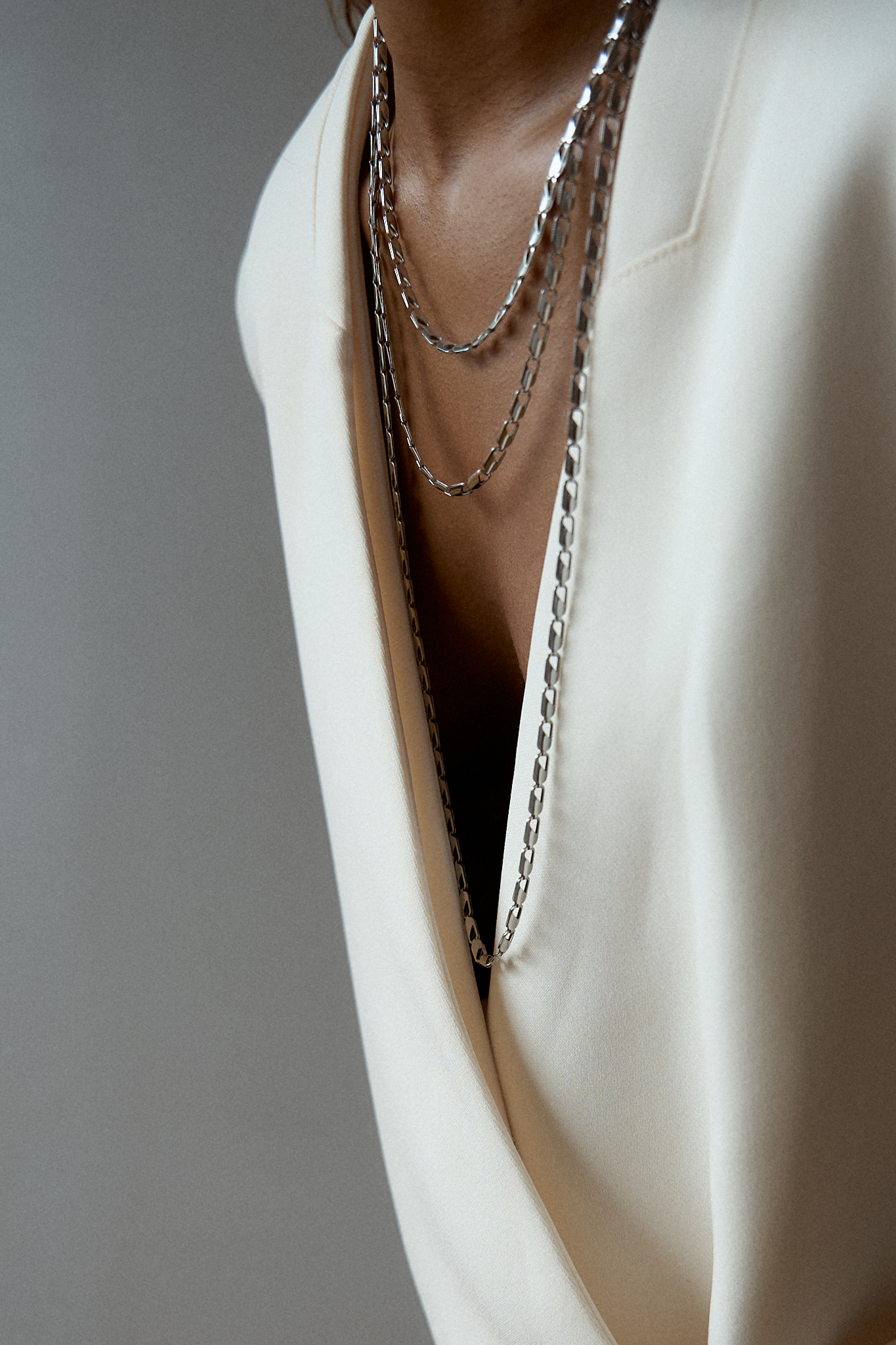 Close-up of a minimalist outfit featuring a structured white blazer and black maxi skirt, detailed with layered silver chain belts and necklaces, highlighting the modern accessories and monochrome palette.