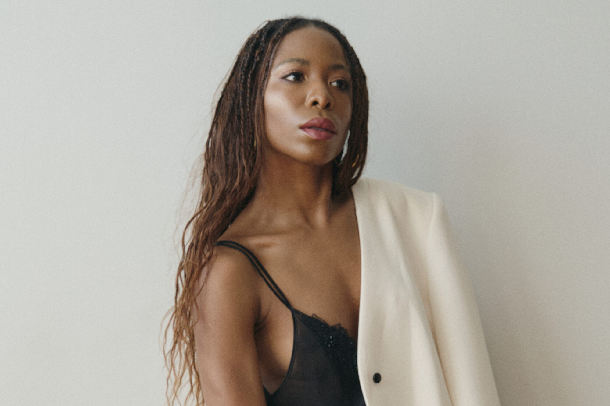 Woman wearing an oversized white blazer paired with a black flowy maxi skirt, styled with layered silver chain belts and silver necklaces, standing confidently against a modern white backdrop.