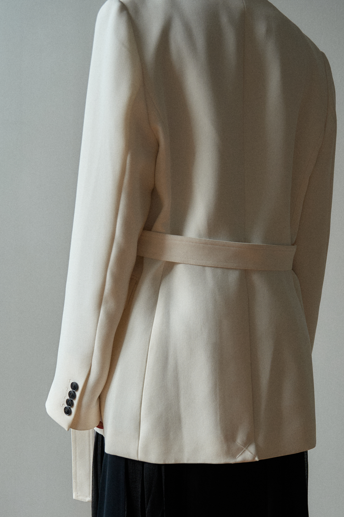 Close-up of a minimalist outfit featuring a structured white blazer and black maxi skirt, detailed with layered silver chain belts and necklaces, highlighting the modern accessories and monochrome palette.