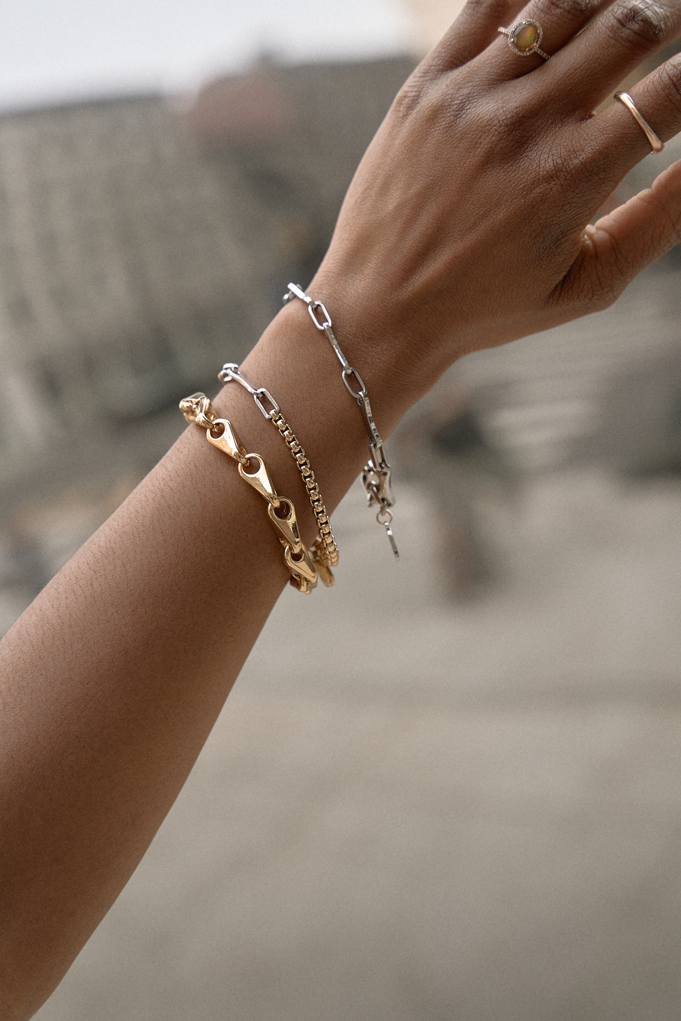 Close-up of a hand adorned with multiple bracelets, including a gold chain link bracelet, a silver chain bracelet, and a delicate silver chain, showcasing a stylish accessory arrangement.