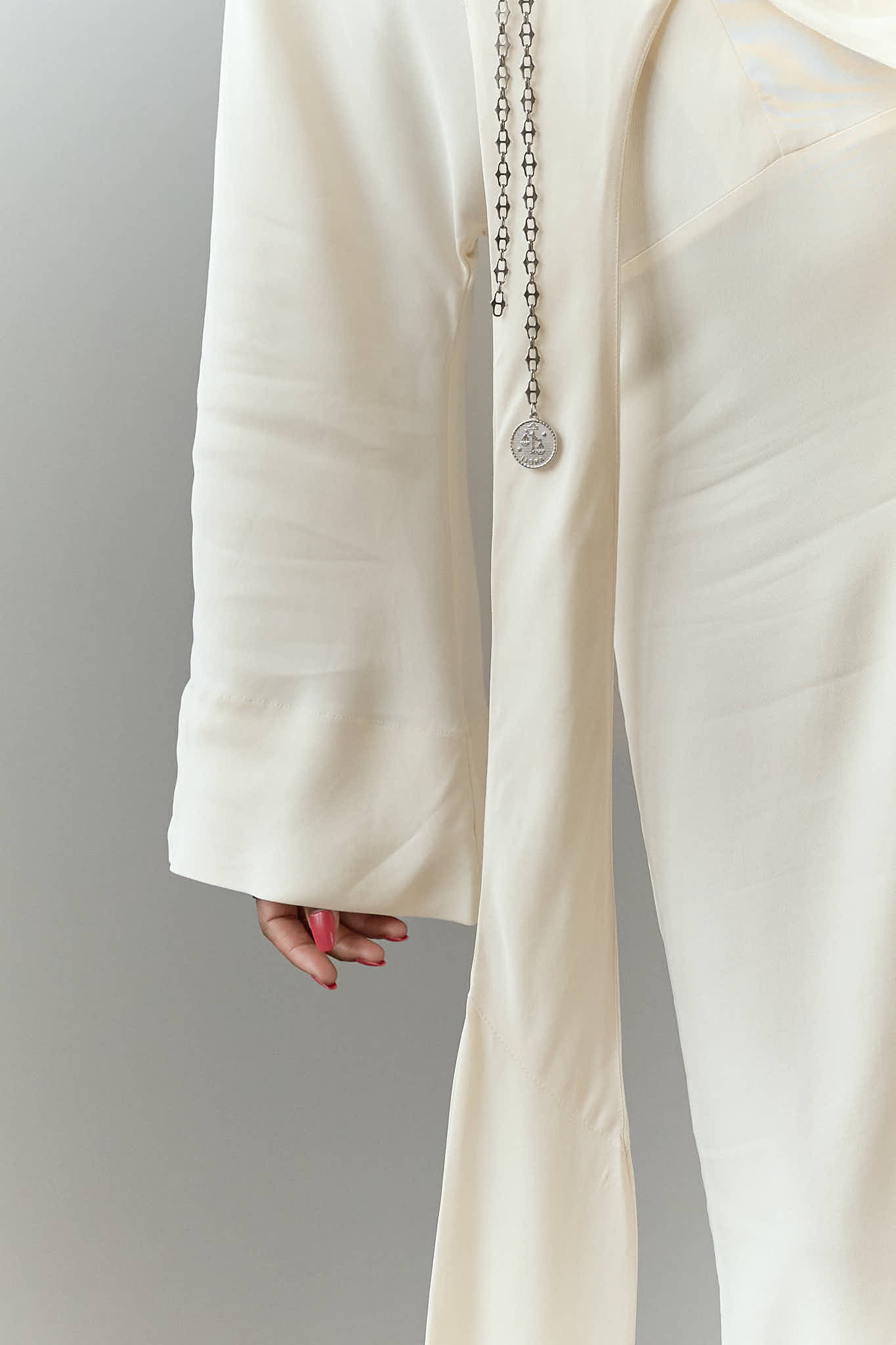 Close up of a silver coin pendant on a long silver lariat chain over a white dress.