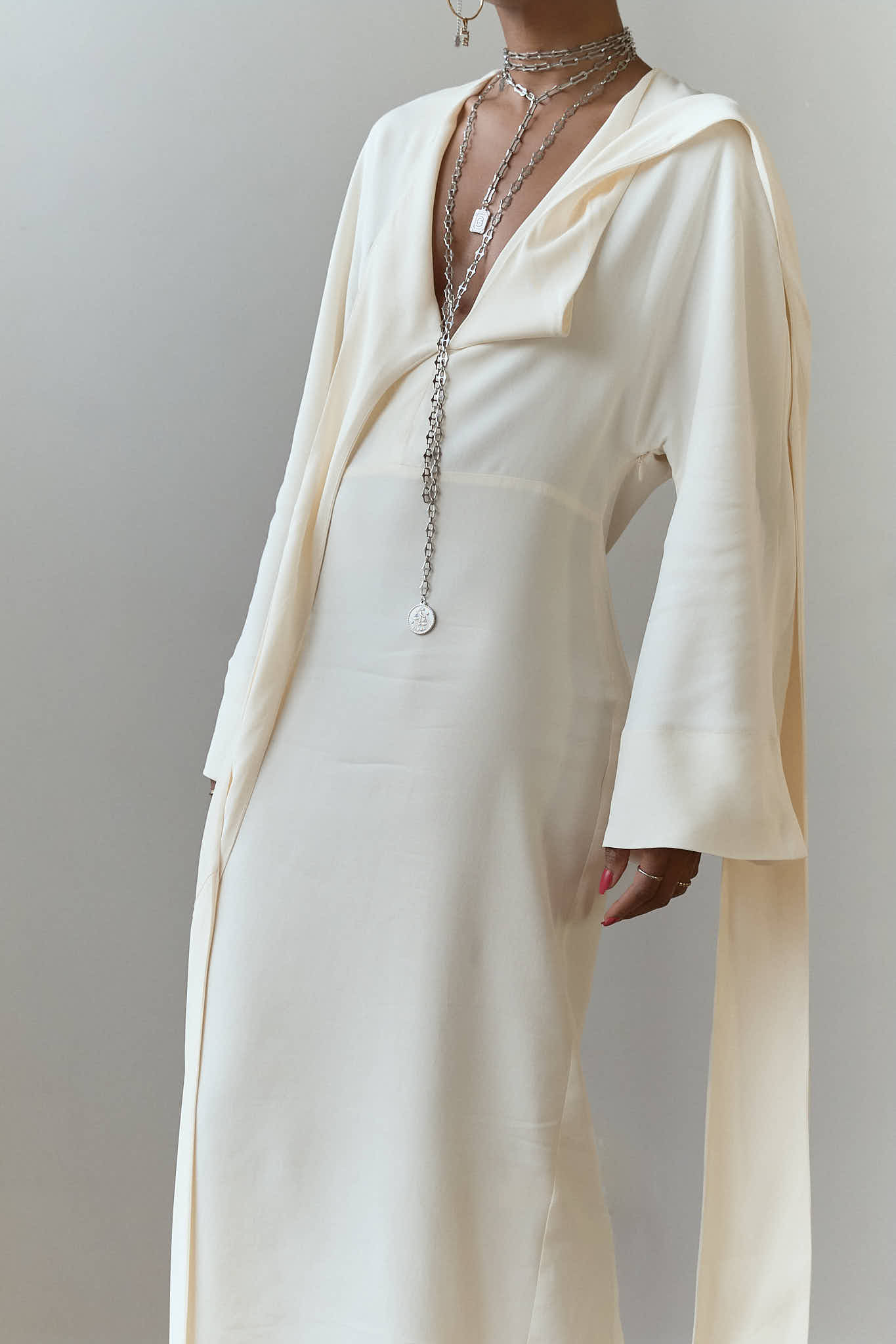 Close up of layered silver jewelry including a chunky choker and coin lariat on a white dress.