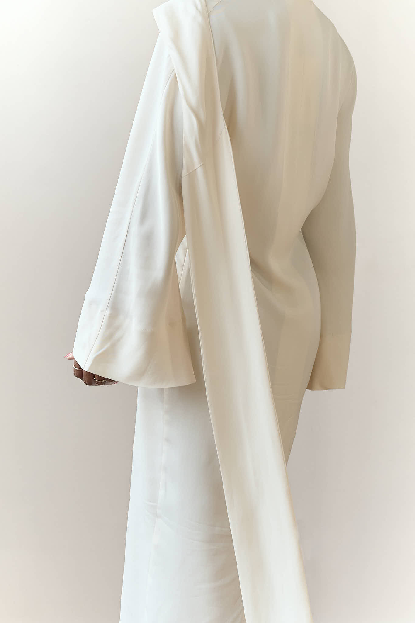Rear view of a white long-sleeve maxi dress, highlighting the fluid, elegant drape of the fabric.