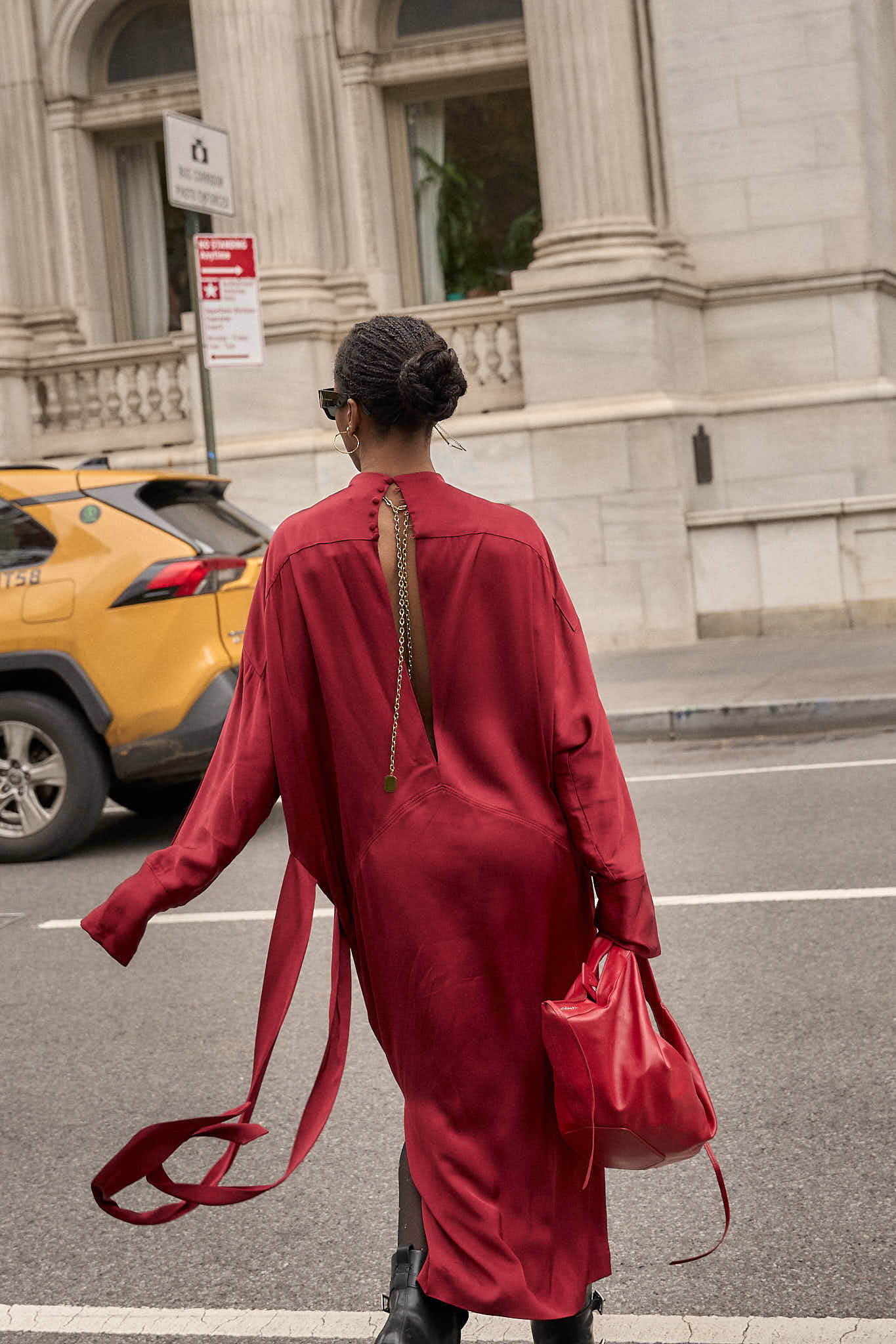 Back view of a flowing red silk dress and black leather moto boots with silver buckle hardware, highlighting the movement of the fabric while walking in new york city.